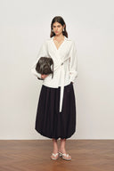 White long-sleeve wrap blouse with tie detail paired with voluminous black bubble skirt, front view on model