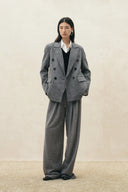 Model wearing grey pleated wide leg wool blend pants with a drawstring waist