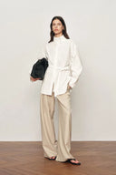 Woman wearing a white oversized belted shirt jacket with a relaxed stand collar, front view on model.