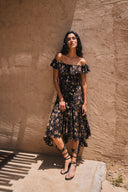 Black viscose floral dress with off-shoulder ruffle neckline and asymmetrical hem, on-model standing front view