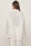 Back view of a white cotton shirt with openwork trim on cuff, relaxed fit, and soft linen texture on model.