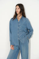 On-model view of a relaxed fit denim shirt in medium blue with a chest pocket and button front closure