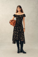 Black viscose dress with handpainted floral print and off-shoulder ruffle, front on-model view with boots and bag