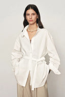 White cotton-blend oversized shirt jacket with belt, relaxed collar, and long sleeves, front view on model.