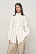White oversized shirt jacket with stand collar and matching belt, front view on model in neutral pants