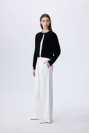 Black lyocell-wool blend knit cardigan with pearl neckline embellishment, front view on model with white pants