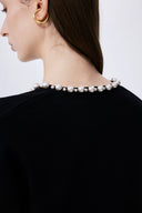 Close-up of black lyocell-wool blend cardigan back neckline adorned with graduated pearl embellishments on model.