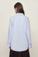 Back view of pale blue cotton shirt with openwork trim on cuffs and relaxed silhouette