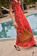 Red sleeveless dress with cowl neck and floral jacquard pattern, side view on model near poolside