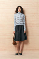 Model wearing a dark belted pleated midi skirt with a light knit cardigan and black flats