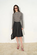 Woman wearing a black belted pleated midi skirt with a plaid blouse and black handbag