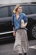 Woman wearing a sky blue Lyocell denim shirt with rolled sleeves and a plaid midi skirt walking outdoors