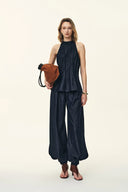 Woman wearing a dark denim halter top and wide leg jeans set with a brown shoulder bag