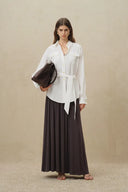 White belted linen blend blouse with roll tab sleeves, front view styled with dark pleated maxi skirt and bag.