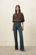 Model wearing high waist washed denim flare jeans with buckle pockets and split hems