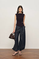Sleeveless black twisted drape top with side embellishment paired with loose dark cotton-blend pants, front view on model