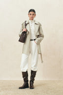 Woman wearing a champagne belted oversized cropped trench coat with white pants and tall brown boots