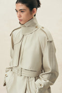 Woman wearing a champagne belted cropped trench coat with a high collar and oversized sleeves