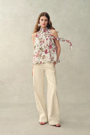 Woman wearing a sleeveless stretch silk double crepe floral top with beige pants against a plain background