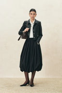 Woman wearing a black elasticated bubble midi skirt with a tailored jacket and shoulder bag