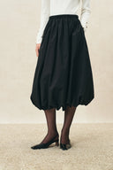 Black elasticated bubble midi skirt with gathered volume and curved hem, styled with a white top and black heels