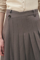 Houndstooth pleated midi skirt with a V cut waistband and sharp asymmetric pleats