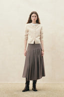 Model wearing a pleated houndstooth wrap midi skirt with an asymmetric hem