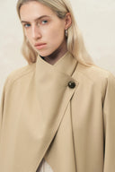 Woman wearing a beige draped wool blend coat with a high collar and single button