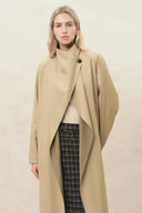Woman wearing a beige draped single breasted wool blend coat with high collar and plaid trousers