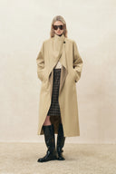 Woman wearing a beige long coat with high collar, plaid skirt and black knee high boots