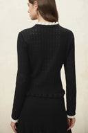 Black crochet openwork cardigan with scalloped hem and long sleeves shown from the back