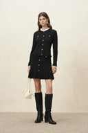 Model wearing a black scalloped cardigan with a ruffled skirt knee high boots and a cream handbag