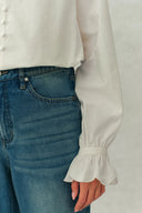 White crinkle cotton blouse with button front and fluted cuffs paired with blue jeans