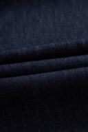 Close up of dark indigo cotton denim fabric with a textured weave and layered folds