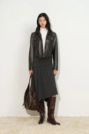 Woman wearing a fitted washed vegan leather biker jacket with a pleated skirt and tall boots