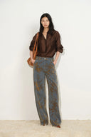 Model wearing floral flocked jacquard barrel leg jeans in blue denim with a brown shirt