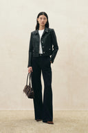 Model wearing a black cropped vegan leather blazer with softly squared shoulders and tailored trousers carrying a handbag