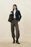 Woman wearing a black cropped vegan leather blazer with softly squared shoulders, brown trousers and ankle boots