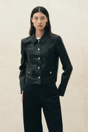 Model wearing a black cropped vegan leather blazer with a shirt collar, metal buttons, and patch pockets