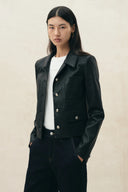 Model wearing a black cropped vegan leather blazer with patch pockets, white top and dark jeans
