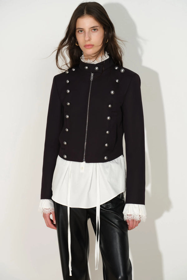 Black fitted Napoleon jacket with double rows of silver buttons over a white blouse and leather trousers