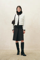 Model wearing a cropped shimmer check wool tweed jacket with welt pockets a black skirt and knee high boots