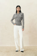Woman wearing a grey cinched waist polo knit top with long sleeves and white trousers