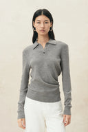 Model wearing a grey cinched waist polo knit top with long sleeves and white trousers